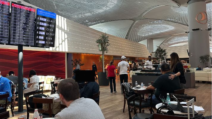 イスタンブール空港のTurkish Airlines Business Lounge内の様子。広いダイニングエリアと出発案内板があり、多くの利用者で賑わっている